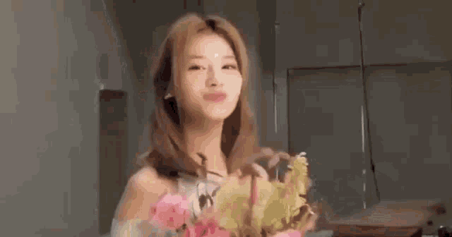 a woman is standing in a room holding a bouquet of flowers and smiling .