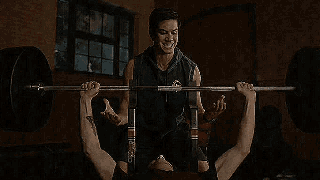 a man is teaching another man how to lift a barbell on a bench .