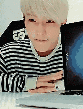 a young man in a striped shirt is sitting in front of a laptop .