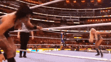two women are wrestling in a wrestling ring with a referee in the background .