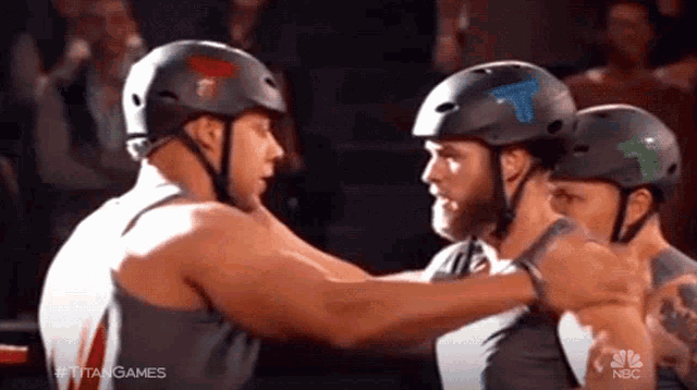 three men wearing helmets are hugging each other and nbc is behind them