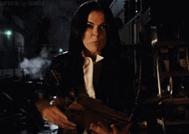 a woman in a black jacket is holding a book and making a hand gesture