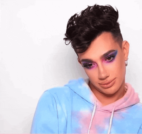 a man with makeup on his face is wearing a tie dye hoodie and earrings