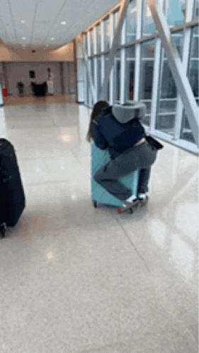 a woman is sleeping on a suitcase in an airport hallway
