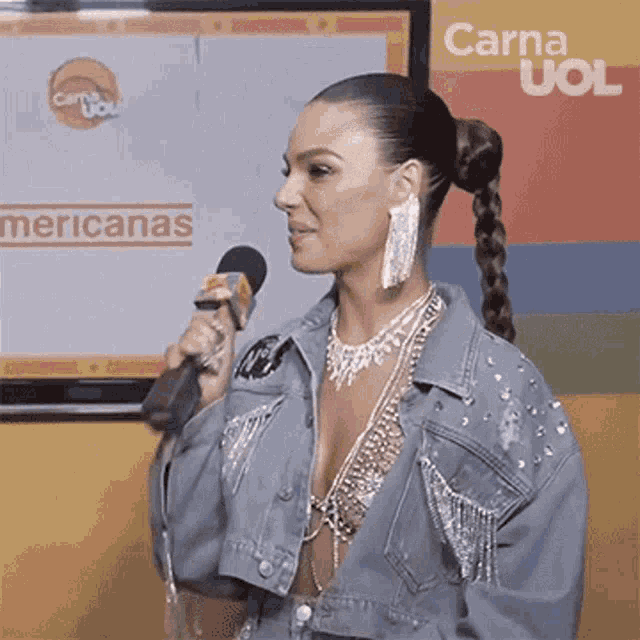 a woman in a denim jacket is holding a microphone in front of a screen that says carna uoi