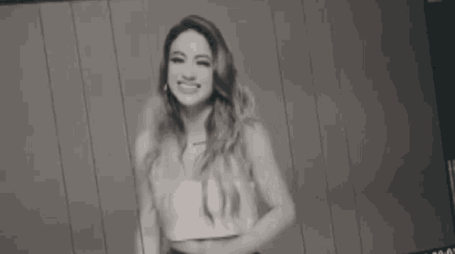 a black and white photo of a woman standing in front of a camera smiling .
