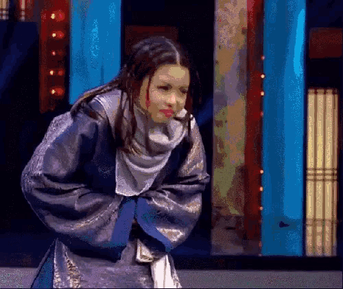 a woman in a blue and gold costume is standing on a stage with her arms crossed .