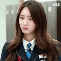 a woman in a school uniform with a blue tie is looking at the camera .