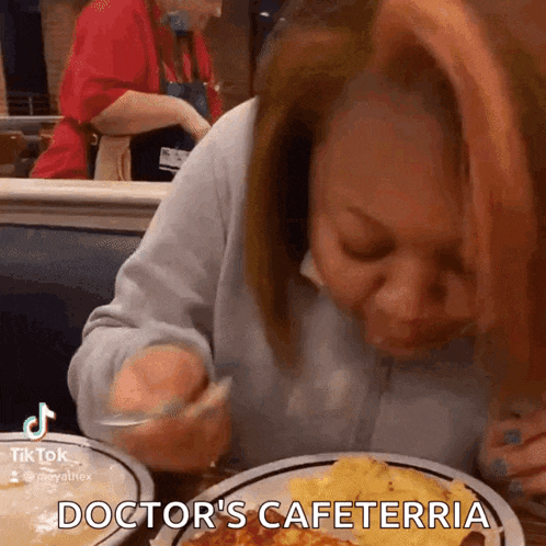 a woman sitting at a table with a plate of food that says doctor 's cafeteria on it
