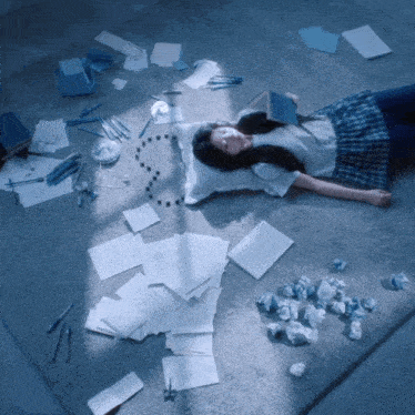 a girl laying on the floor surrounded by papers and a clock