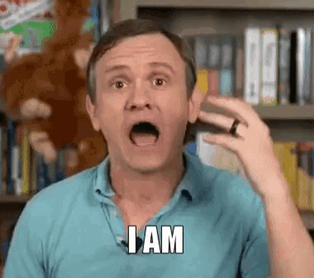 a man in a blue shirt is saying i am in front of a bookshelf .