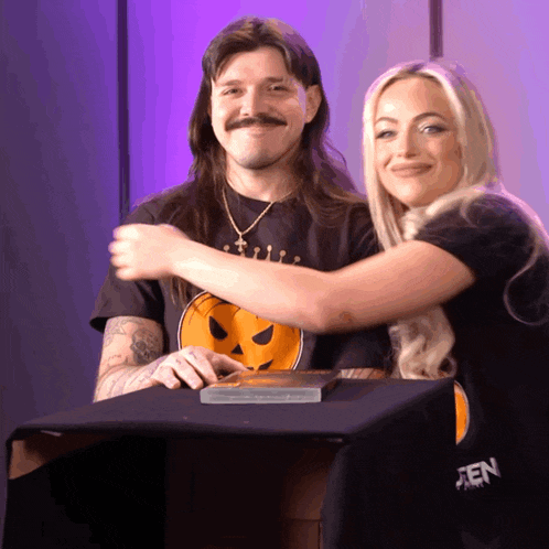 a man and a woman are hugging each other and the woman is wearing a black shirt with a pumpkin on the front