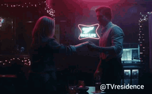 a man and woman are dancing in front of a budweiser neon sign