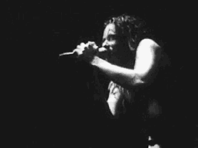 a black and white photo of a woman singing into a microphone on a stage .