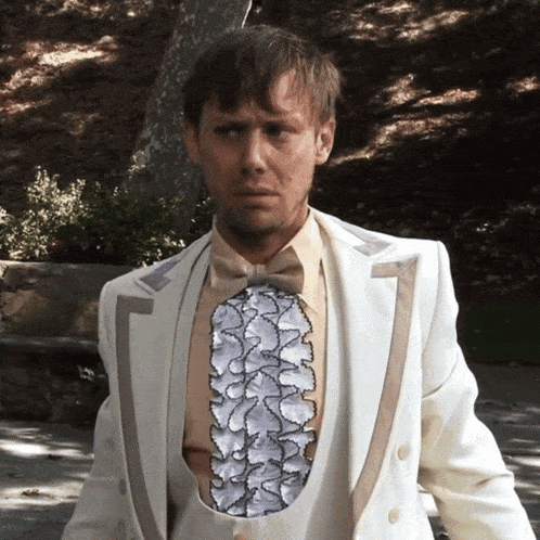 a man in a white suit has a ruffled vest