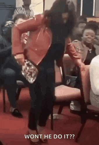 a woman in a red jacket is standing in front of a group of people and holding a purse .