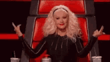 a woman is sitting in a red chair with her arms outstretched and making a peace sign .