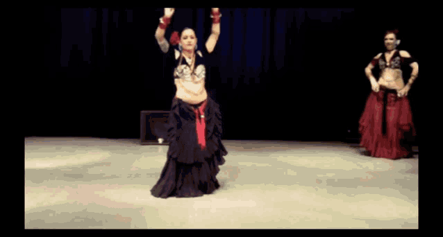 two belly dancers are performing on a stage with a blue curtain in the background