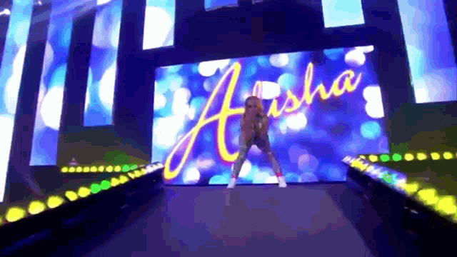 a woman is dancing in front of a large screen that says asha