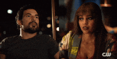 a man covering his mouth while a woman looks at him with a cw logo in the background