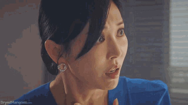 a woman in a blue shirt and earrings is making a funny face .