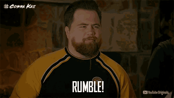 a man with a beard wearing a yellow and black shirt says rumble
