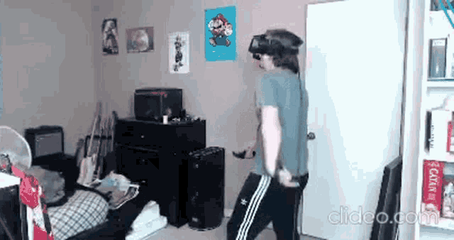 a man wearing a virtual reality headset is standing in a room with a mario poster on the wall .