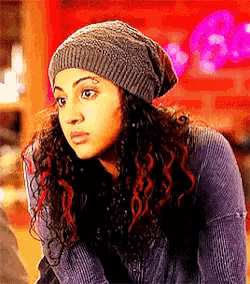 a woman with curly hair wearing a beanie and a sweater is looking at the camera .