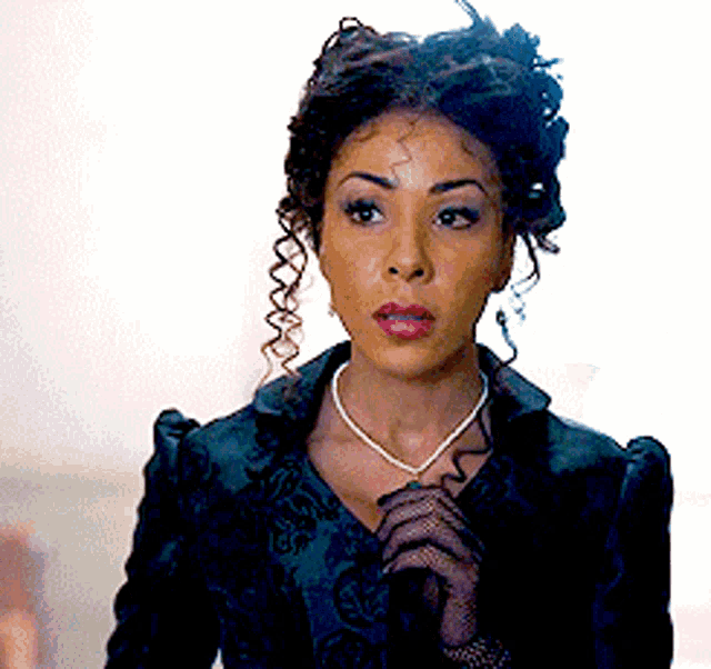 a woman with curly hair is wearing a black jacket and a necklace