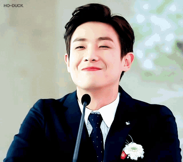 a man wearing a suit and tie is smiling in front of a microphone with the watermark ho-duck