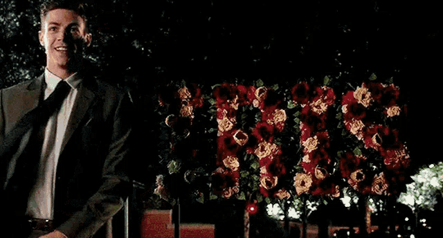 a man in a suit and tie is smiling in front of a display of flowers .