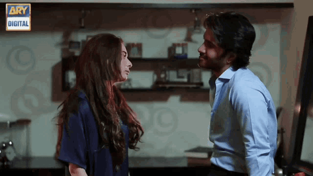 a man and a woman are looking at each other with ary digital in the background