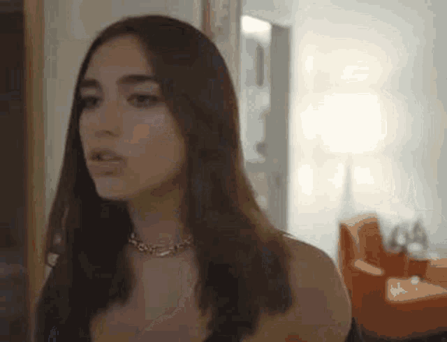 a woman is standing in a room wearing a choker necklace and looking at the camera .
