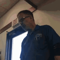 a man in a blue shirt is standing in front of an exit sign