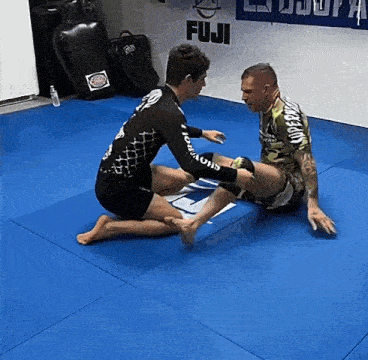 two men are kneeling on a blue mat in front of a sign that says " fuji "
