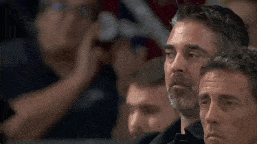a man with a beard is sitting in the stands watching a game