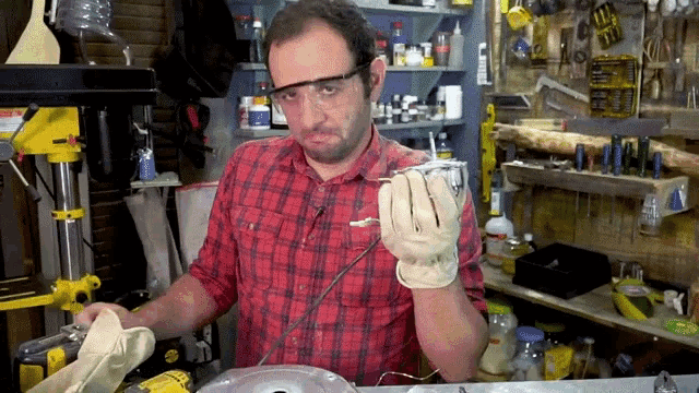 a man wearing a plaid shirt and goggles holds a piece of metal