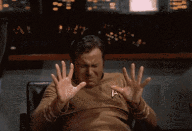 a man in a star trek uniform is sitting in a chair with his hands outstretched and a surprised look on his face .