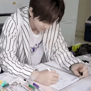 a young man is sitting at a desk writing in a notebook .