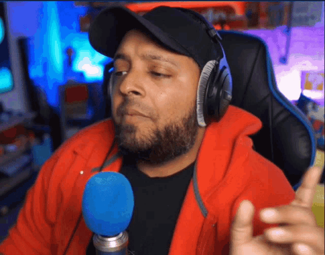 a man wearing headphones and a red jacket is speaking into a blue microphone