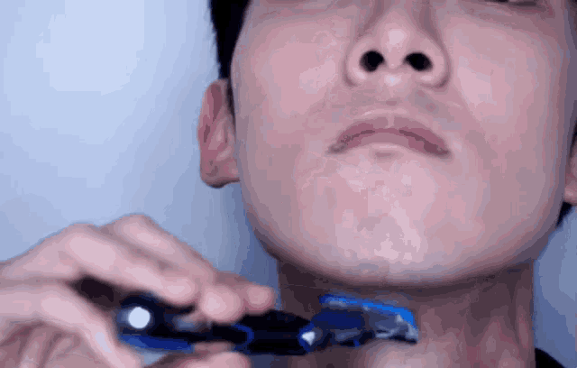 a man is shaving his face with a blue razor
