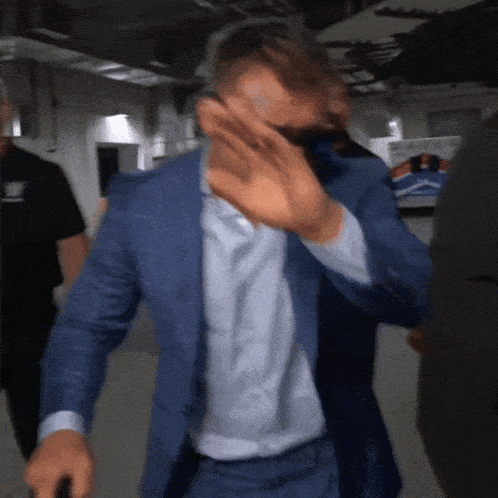 a man in a blue suit and white shirt covering his face with his hand