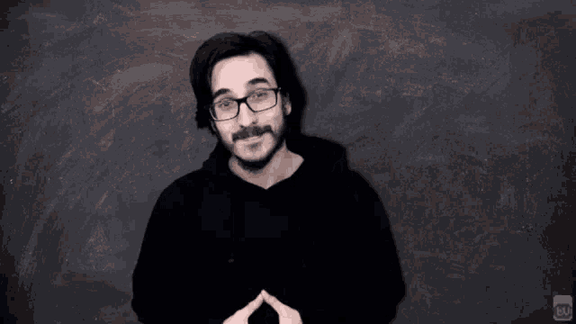 a man with glasses is standing in front of a blackboard .