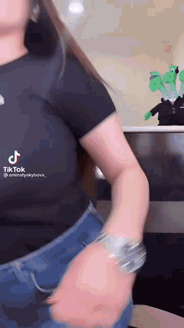 a woman in a black shirt and blue jeans is dancing in front of a table with stuffed animals on it .