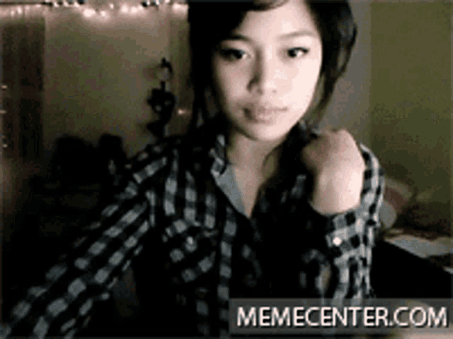 a girl in a plaid shirt is standing in front of a memecenter.com banner