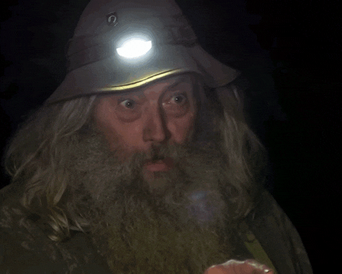 a man with a beard wearing a hat with a light on his head and the words he outfoxed us below him