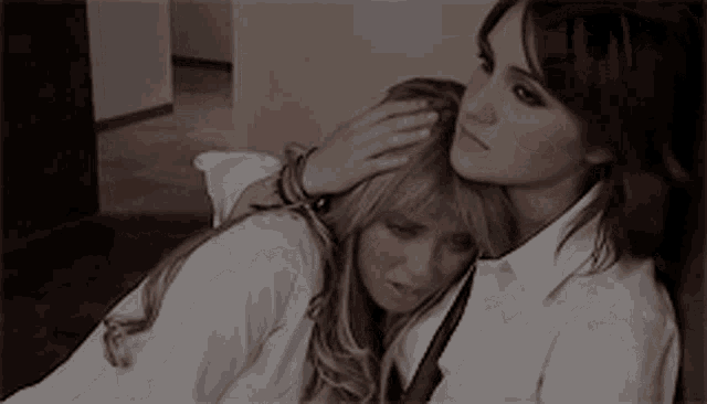 two women are hugging each other and one is putting her hand on the other 's forehead