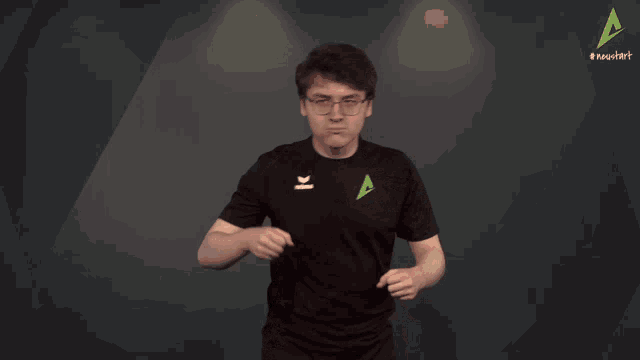 a man wearing glasses and a black shirt is standing in front of a green triangle with the letter a on it