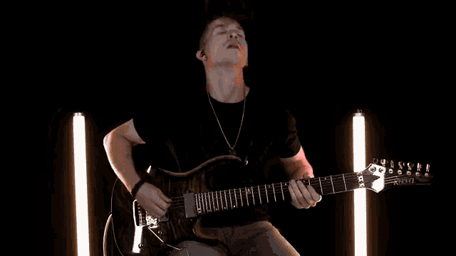 a man is playing a guitar in a dark room with lights behind him .