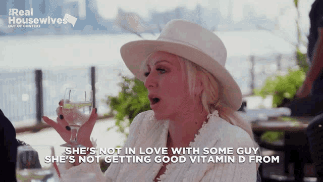 a woman in a white hat is holding a glass of water and says she 's not in love with some guy